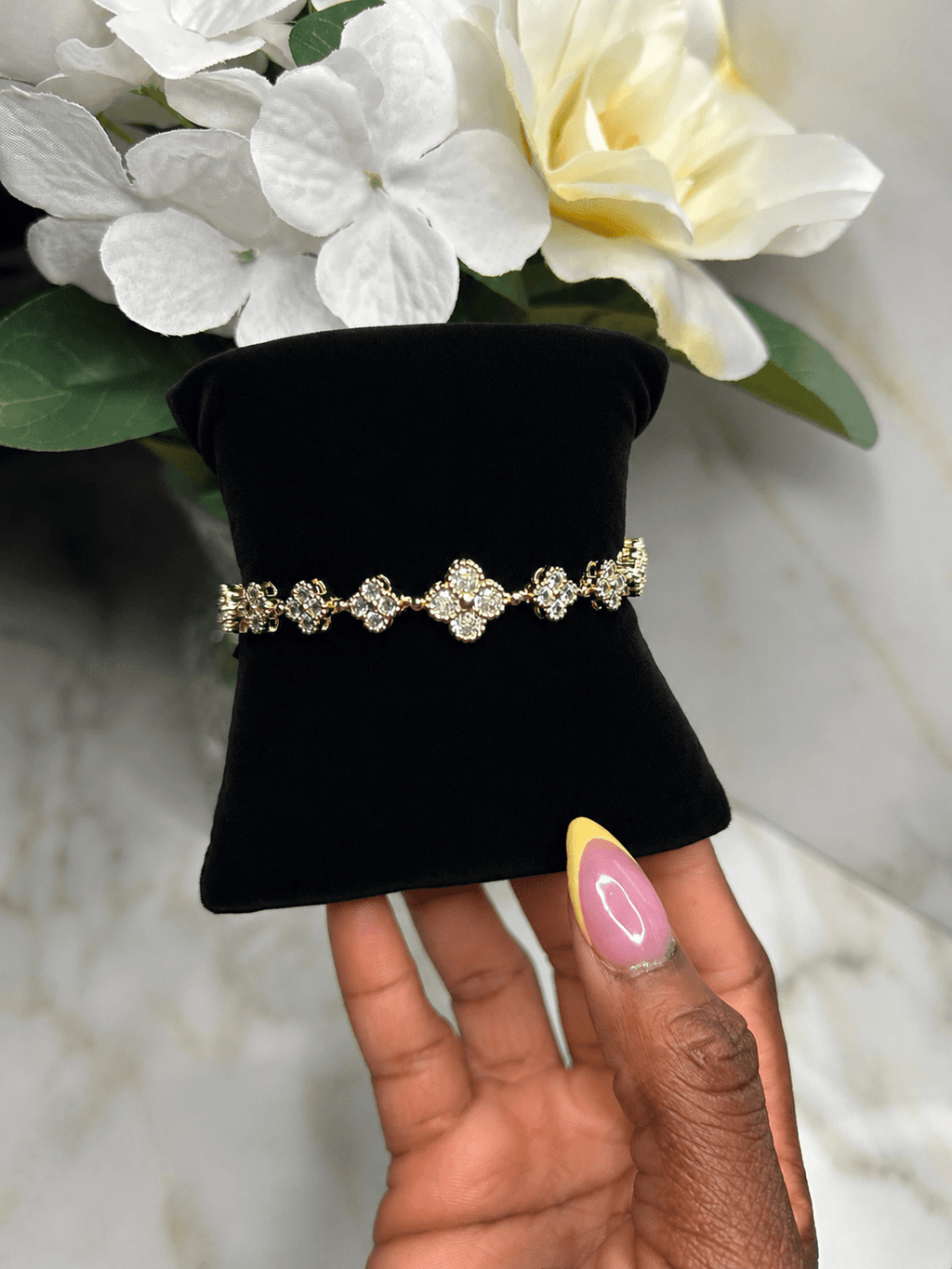 The Blossom Tennis Bracelet displayed on a black velvet stand with a hand holding it, showcasing its sparkling design.