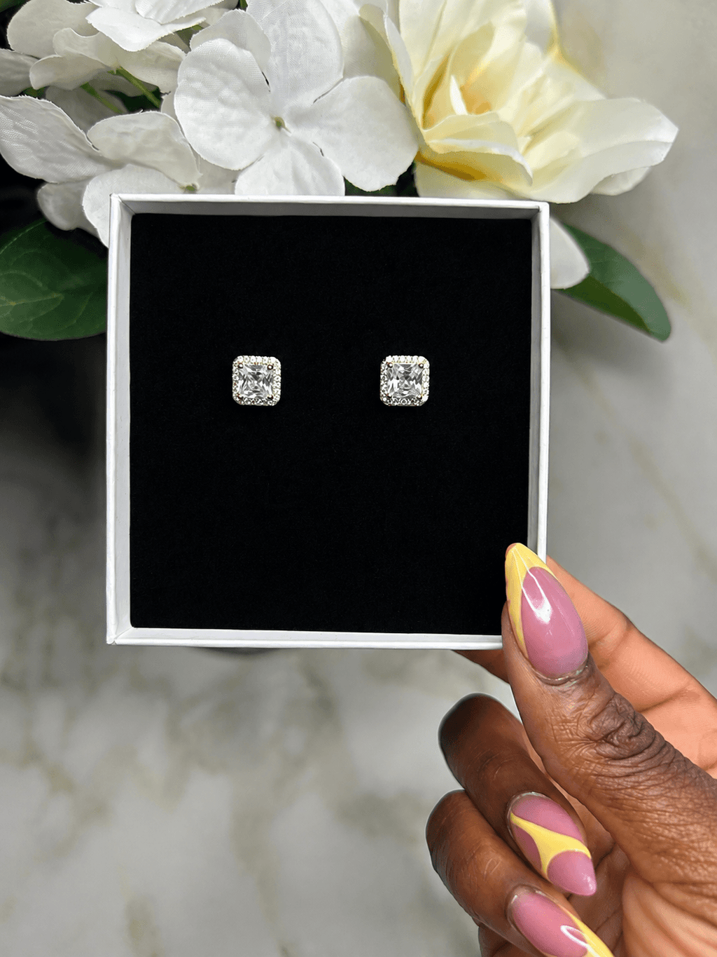 The Reign Diamond Studs showcased in a stylish box with a flower background.
