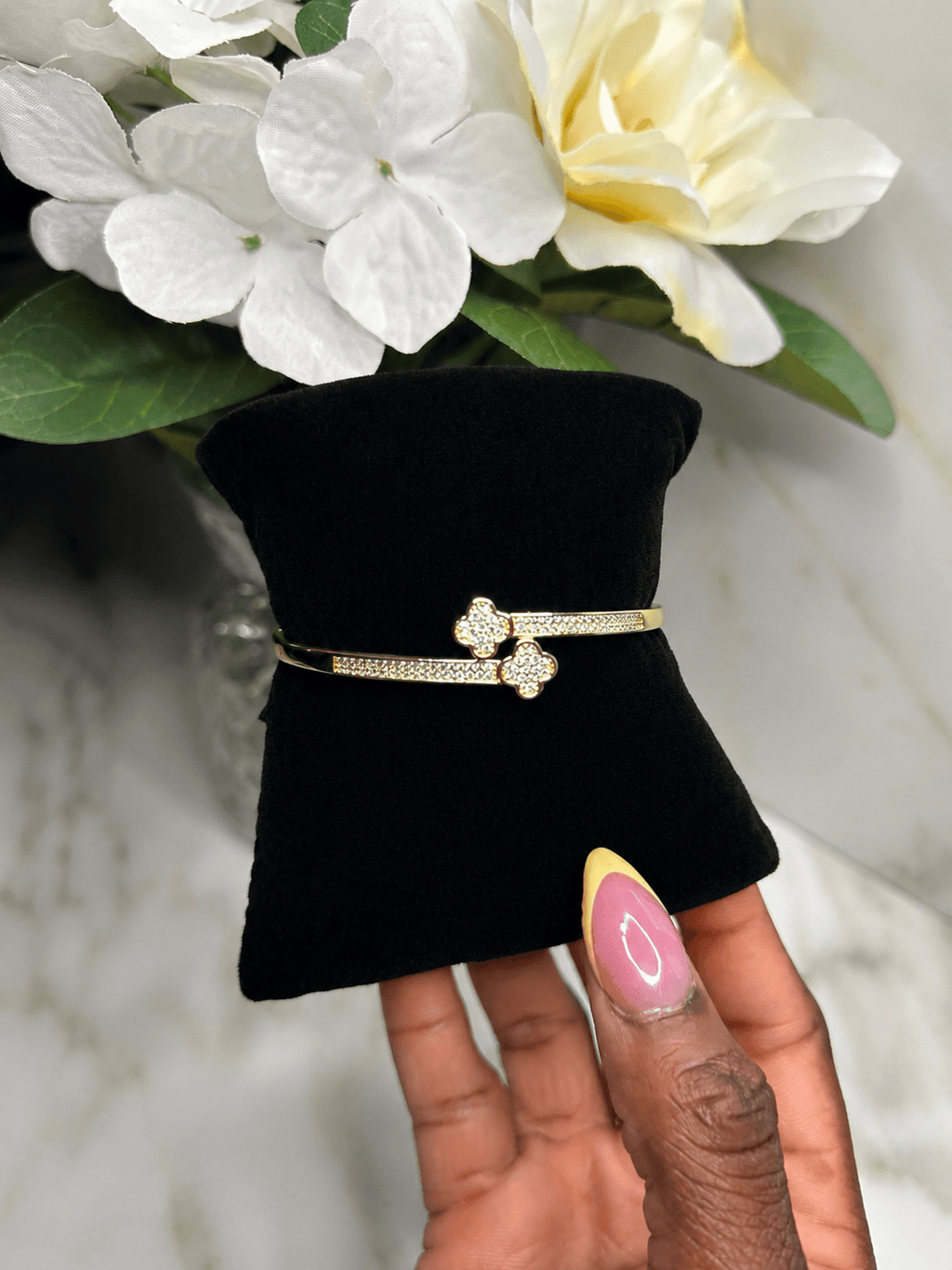 Evermore Double Clover Bracelet showcased on a black display with flowers in the background, symbolizing love and luck.