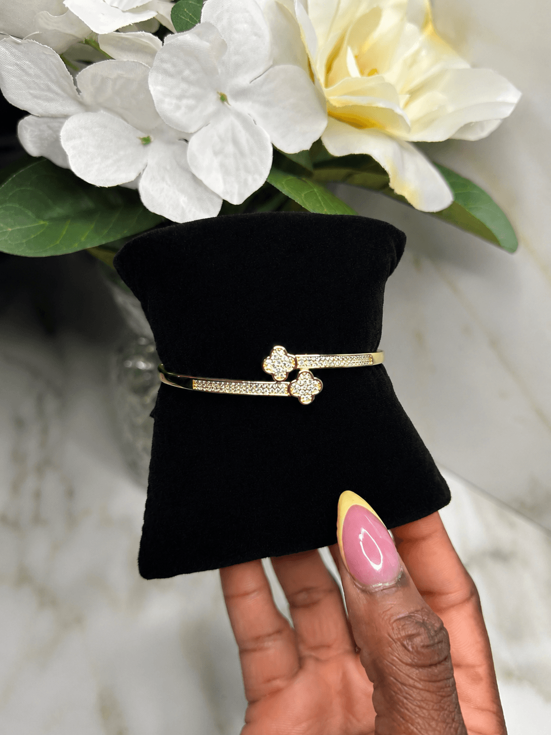 Evermore Double Clover Bracelet showcased on a black display with flowers in the background, symbolizing love and luck.