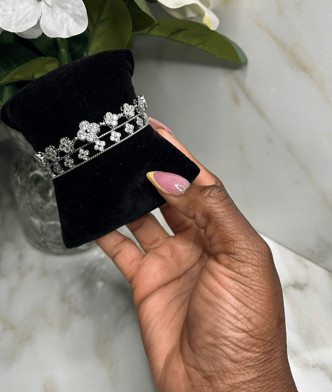 A hand holding The Silver Clover Reign Stack bracelet on a black display pillow with a marble backdrop.