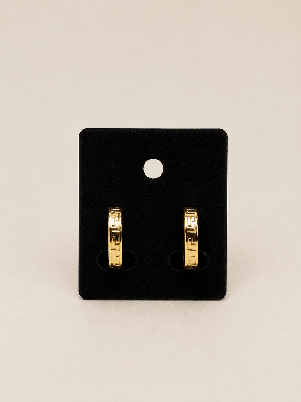 A pair of gold hoop earrings displayed on a black rectangular jewelry card against a light beige background.